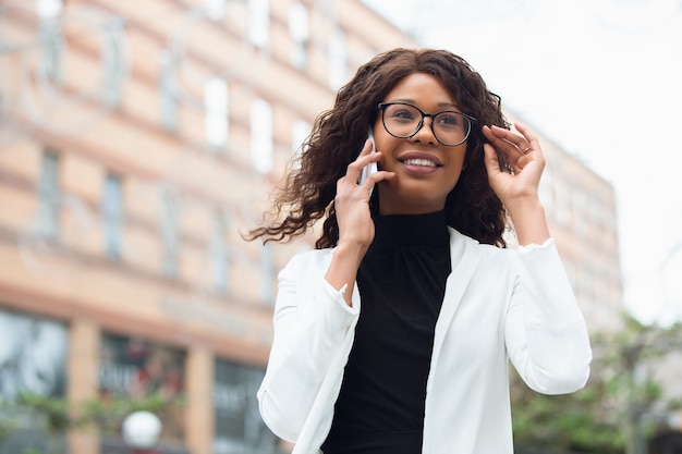 Talking phone. African-american businesswoman in office attire smiling, looks confident and serious, busy. Finance, business, equality and human rights concept. Beautiful young model, successful.