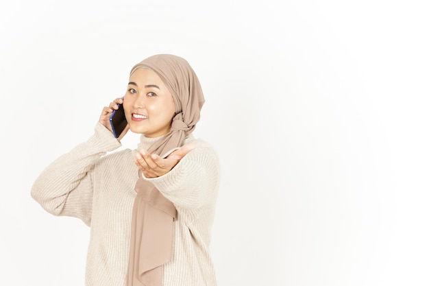Parlando al telefono e allungando la mano di una bella donna asiatica che indossa l'hijab isolata su bianco