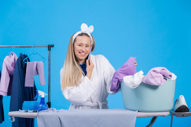 Talking on the phone with a friend while getting ready for work in the morning A smiling girl wearing a robe and a headband is sorting clothes ironing them