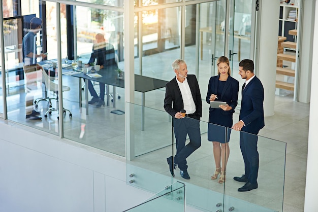 Talking strategy before the meeting Shot of three colleagues talking together over a digital tablet while standing in a modern office