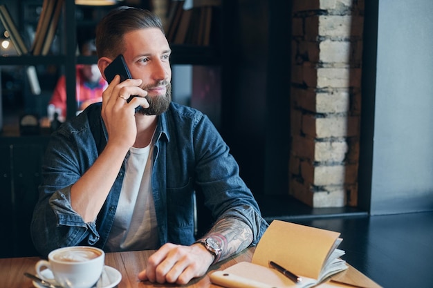 Talking with friends. Confident young man talking on the mobile phone and smiling while sitting in cafe