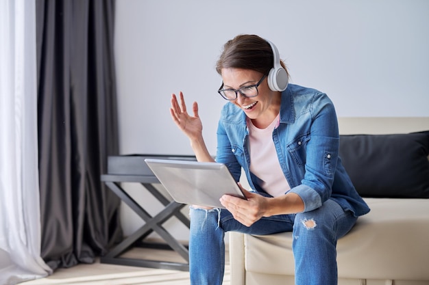 Talking woman in headphones looking into digital tablet webcam