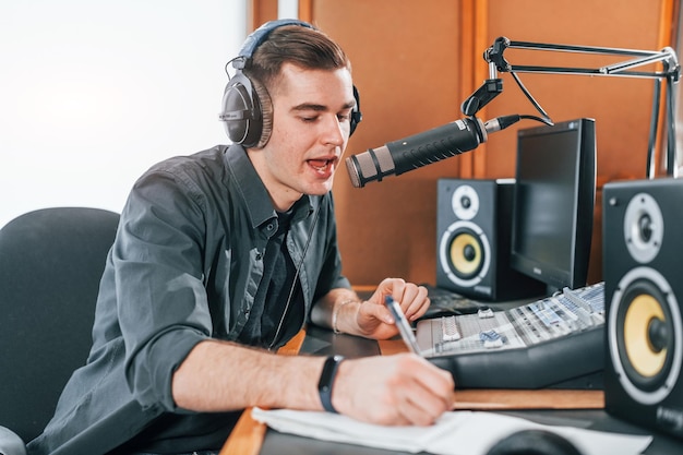 대화하고 마이크를 사용하는 청년은 실내에 있는 라디오 스튜디오에서 방송으로 바쁘다