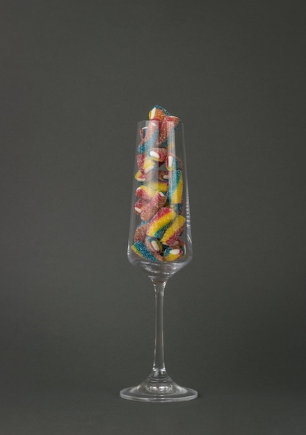 Высокий стеклянный стакан, наполненный сахарным мармеладом на сером фоне.