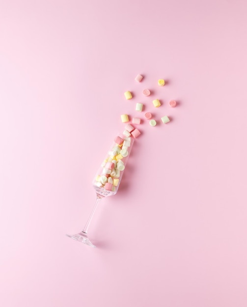 A tall glass glass with crumbling multicolored marshmallows on a pink background. The concept of Valentine's Day. Flat lay.