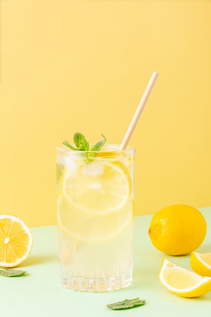 Tall glass of ice tea with lemons around and mint leaves on yellow and mint background