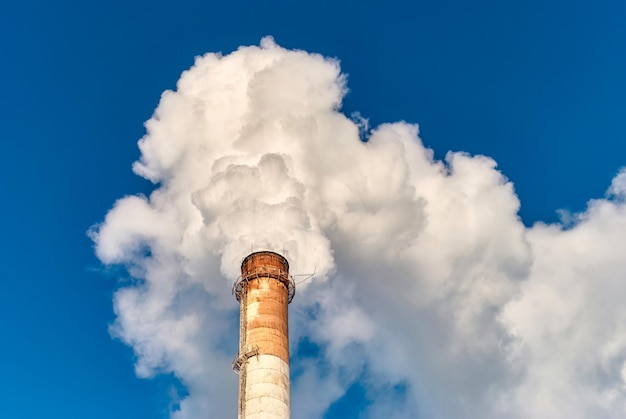 Tall grungy factory pipe emitting thick white fume against cloudless blue sky