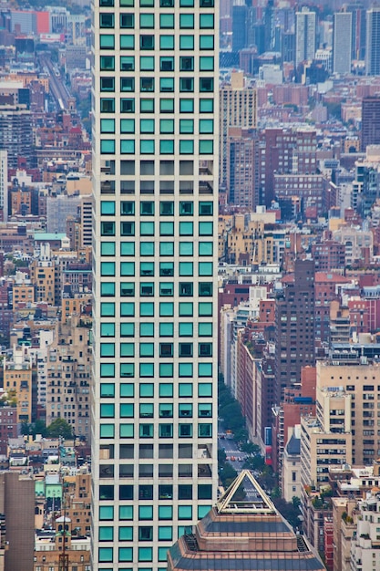 Tall narrow skyscraper of turquoise squares with background of small buildings from above vertical