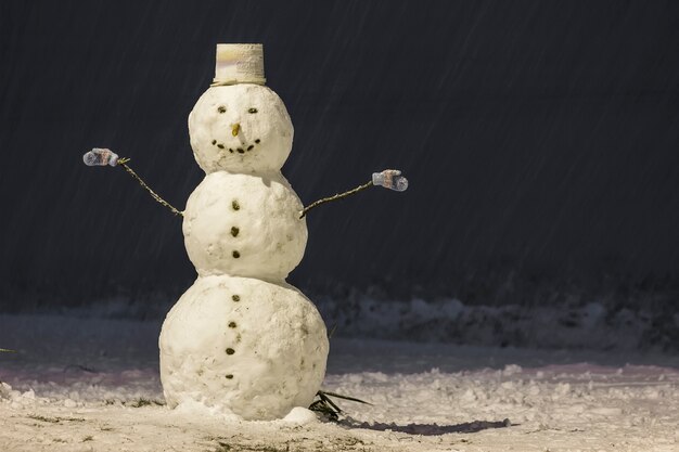 Tall snowman at winter night in the park outdoors.