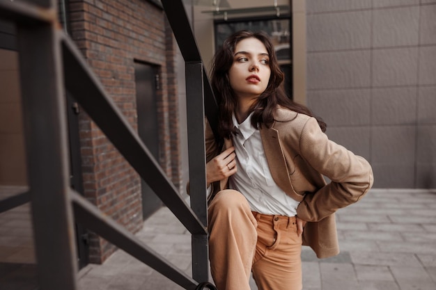 tall stylish girl with oversized jacket posing near the railing and steps on the city background