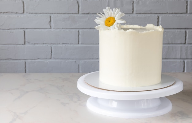 Photo tall white cake on a stand with a decor of a chamomile flower.