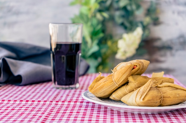 Tamales served on a traditional table with a glass of red wine. A typical sandwich or Latin American meal of cornmeal and meat. Traditional Andean food. Traditional food concept