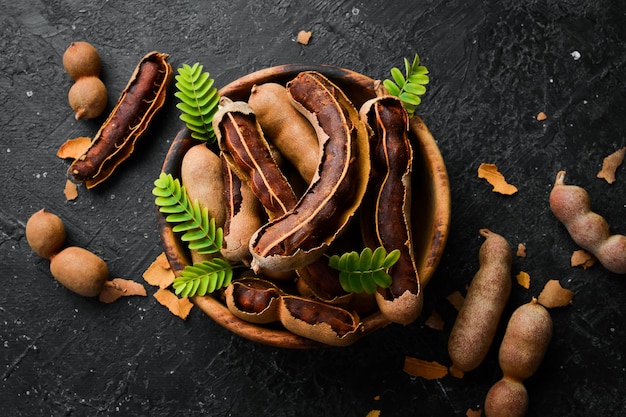 Tamarind tropical fruits with leaf in a wooden bowl On a stone background