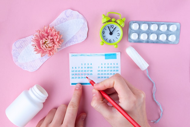 Photo tampon, feminine, sanitary pads for critical days, feminine calendar, alarm clock, pain pills during menstruation and a pink flower. care of hygiene during menstruation