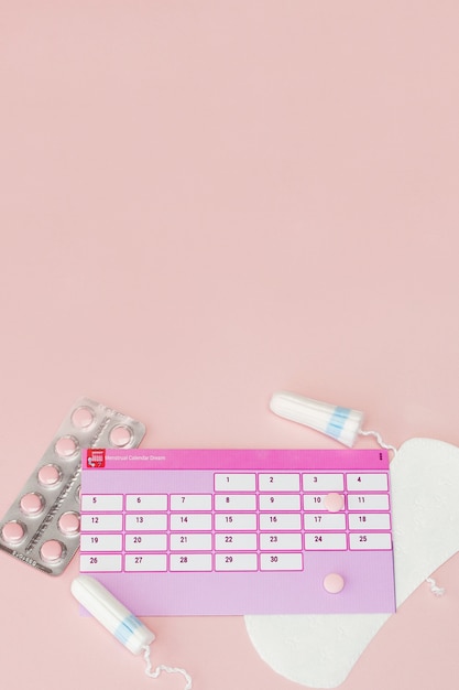 Tampon, feminine, sanitary pads for critical days, feminine calendar, pain pills during menstruation on a pink wall. Tracking the menstrual cycle and ovulation