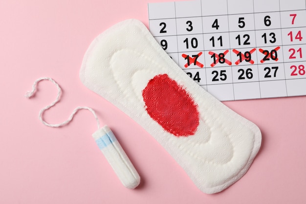 Photo tampon, used sanitary pad and calendar on pink surface