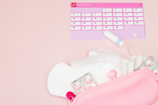 Tampon, vrouwelijk, maandverband voor kritieke dagen, vrouwelijke kalender, pijnstillers tijdens de menstruatie op een roze achtergrond. Het volgen van de menstruatiecyclus en ovulatie