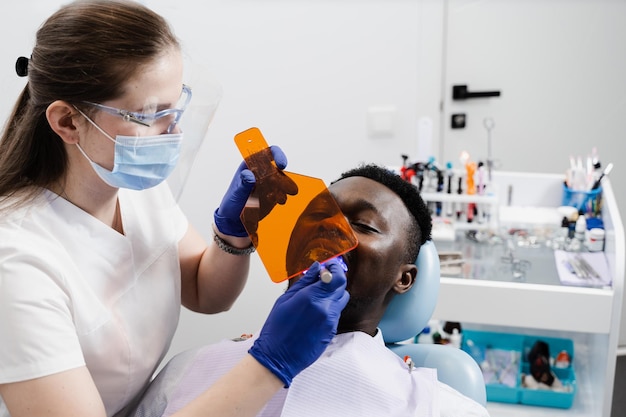 Tandarts behandelt en verwijdert cariës bij Afrikaanse man patiënt Uv-verlichting van fotopolymeer tandvulprocedure bij tandheelkunde