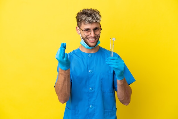 Tandarts blanke man met tools geïsoleerd op gele achtergrond geld gebaar maken