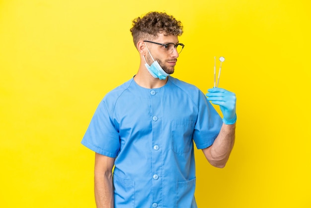 Tandarts blonde man met tools geïsoleerd op de achtergrond op zoek naar de kant