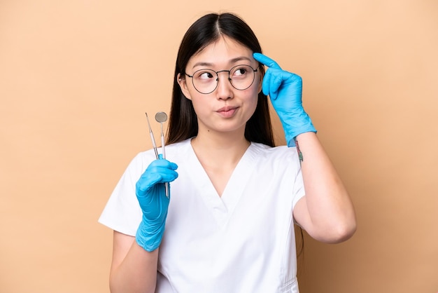 Tandarts Chinese vrouw met tools geïsoleerd op beige achtergrond met twijfels en denken