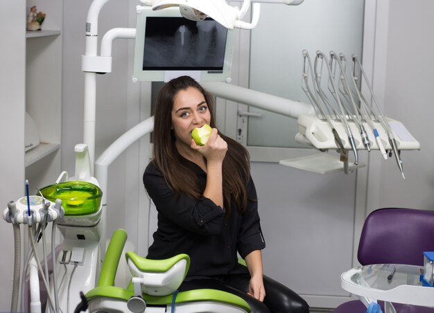 Tandarts concept. gelukkige patiënt in tandartsstoel die groene appel eet