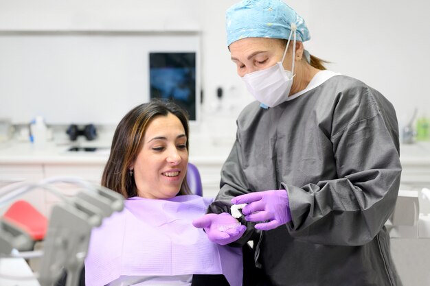 Tandarts die aan vrouwenpatiënt een orthodontische siliconetrainer toont. mobiel orthodontisch apparaat voor gebitscorrectie.