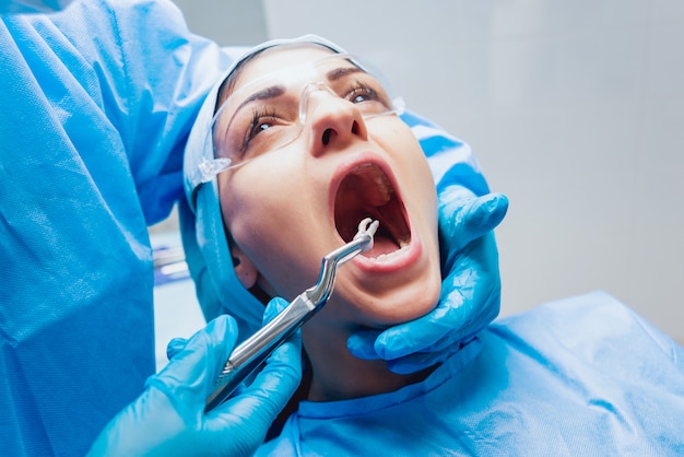 Tandarts die chirurgische tang gebruiken om een rottende tand te verwijderen. Moderne tandheelkundige kliniek