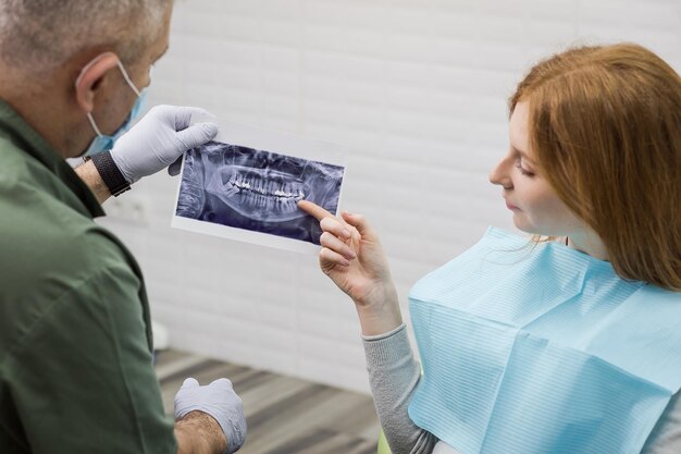 Tandarts die de details van een röntgenfoto van tanden uitlegt aan zijn patiënt in de kliniek