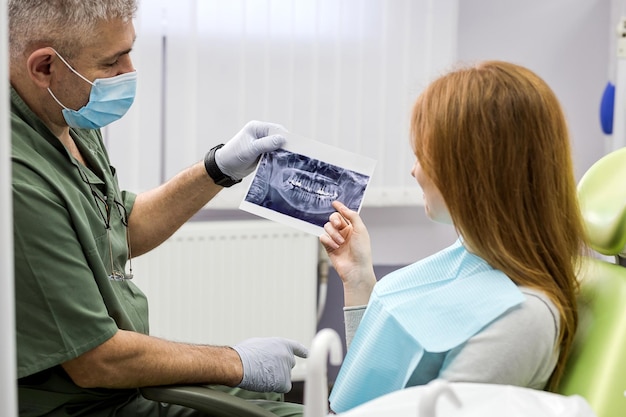 Tandarts die de details van een röntgenfoto van tanden uitlegt aan zijn patiënt in de kliniek