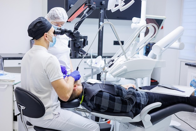 Foto tandarts en assistent controleren de tanden van de patiënt met tandheelkundige hulpmiddelen microscoopspiegel en sonde in het kantoor van de tandheelkundige kliniek concept geneeskunde, tandheelkunde en gezondheidszorg tandheelkundige apparatuur