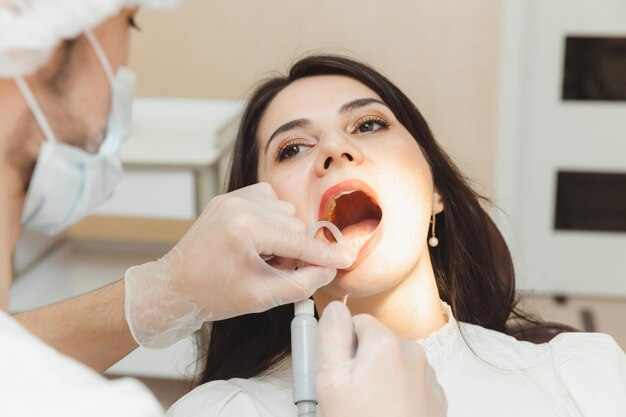 Tandarts en patiënt in de tandartspraktijk De arts behandelt de tanden van een jonge vrouw met een boor Hygiëne en gezonde tanden