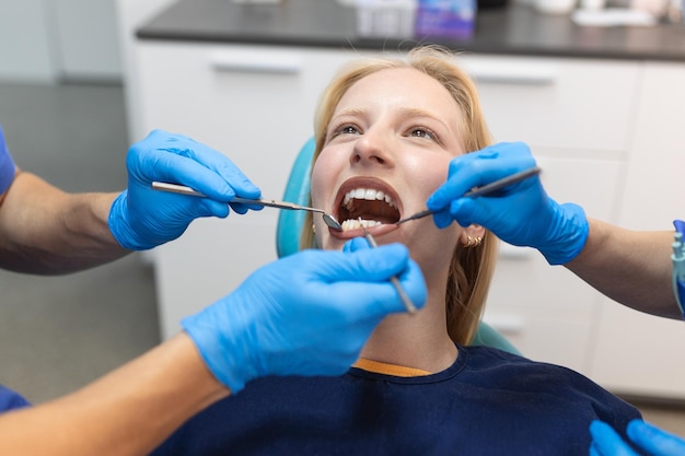 Tandarts in blauw uniform met assistent die tandenprocedure doet aan patiënte vrouwelijke patiënt met turbine tijdens behandelingsprocedure in hedendaagse tandheelkundige kliniek