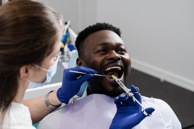 Tandarts injecteert anesthesiespuit van de zieke tanden voor de behandeling van cariës van de Afrikaanse man