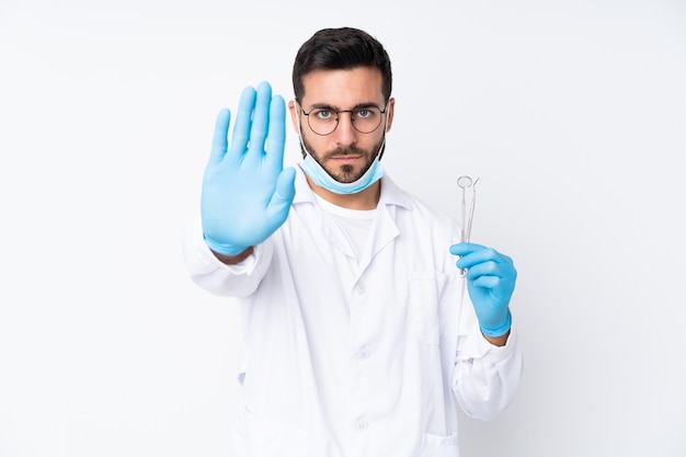 Tandarts man met tools geïsoleerd op een witte muur stop gebaar met haar hand maken