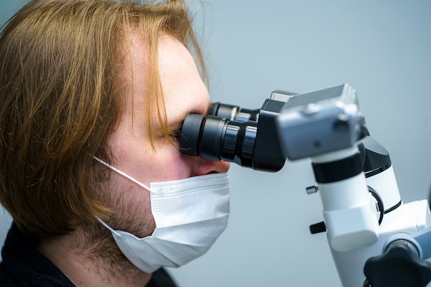 Tandarts met beschermend masker en handschoenen repareren tand van een cliënt bij moderne ambulant met microscoop. Mondverzorging.