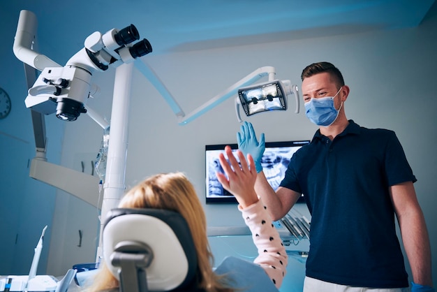 Tandarts met een chirurgisch masker geeft een high-five aan een meisje.