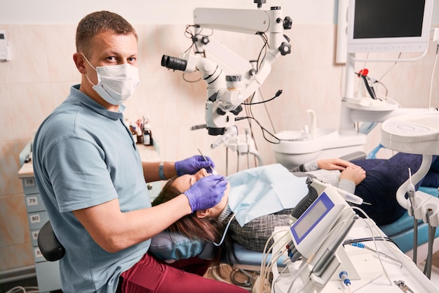 Tandarts met medisch masker die de tanden van de patiënt in de tandartspraktijk onderzoekt