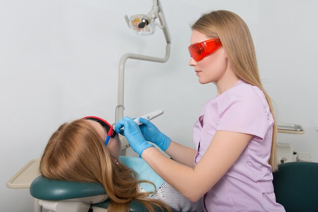 Tandarts met rode bril en apparaat voor tandvullingen behandelt de patiënt die in de stoel zit
