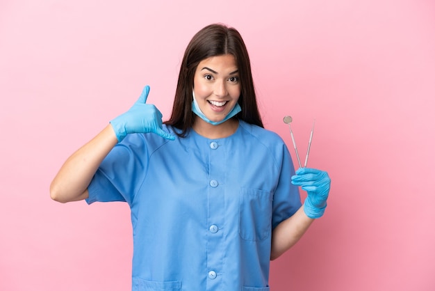 Tandarts vrouw met tools geïsoleerd op roze achtergrond telefoon gebaar maken. Bel me terug teken