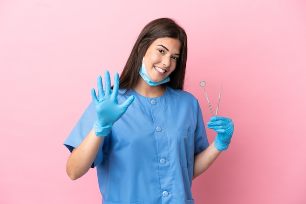 Tandarts vrouw met tools geïsoleerd op roze achtergrond tellen vijf met vingers