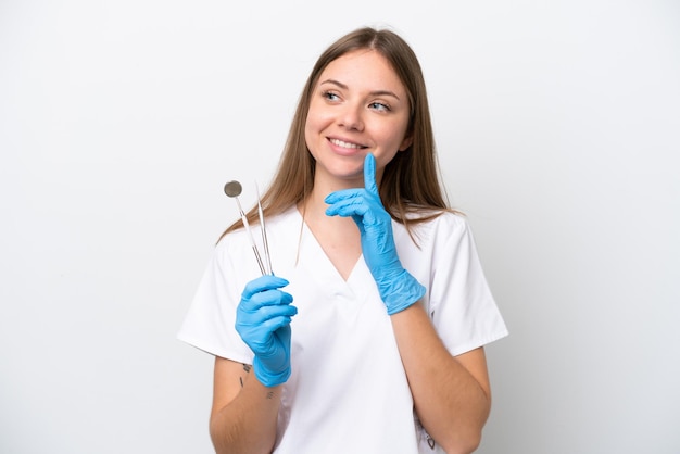 Tandartsvrouw die hulpmiddelen houdt die op witte achtergrond worden geïsoleerd en een idee denkt terwijl ze omhoog kijkt