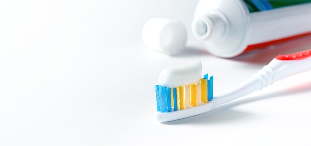 Tandenborstel met witte tandpasta en tube tandpasta op witte achtergrond
