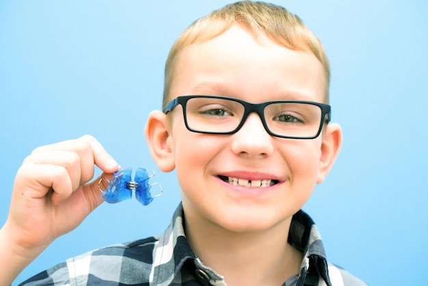 Tandheelkundige orthodontische plaat Uitbreiding van de kaak bij een kind Plaat in de lucht Niet genoeg ruimte voor kiezen Gelukkige jongen met een orthodontische plaat in zijn handen