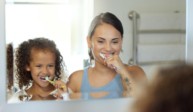 Tandheelkundige zorg tanden poetsen en gezonde routine in moeder en dochter ochtend thuis Gelukkig leuk en speels kind en ouder binding en leren hygiëne en verzorging met tandpasta in een badkamer