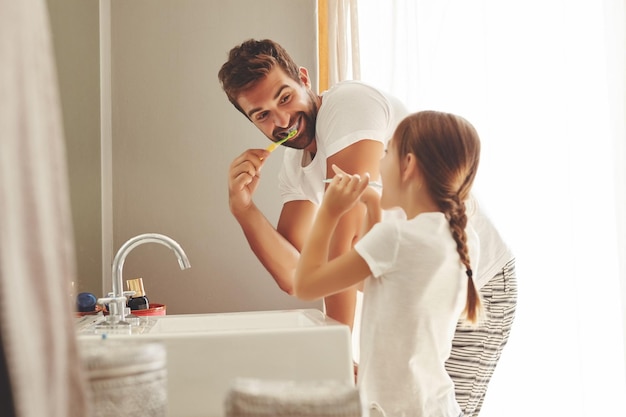 Tandheelkundige zorg vader en dochter poetsen hun tanden en in de badkamer van hun huis Mondhygiëne routine ouder met kind tandenborstel gebruiken voor gezondheid en welzijn mondbescherming in de ochtend