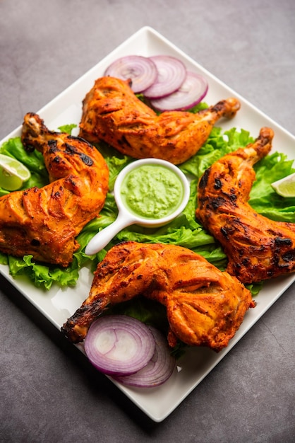 Tandoori chicken is a chicken dish prepared by roasting chicken marinated in yogurt and spices in a tandoor or a clay oven, served with onion and green chutney