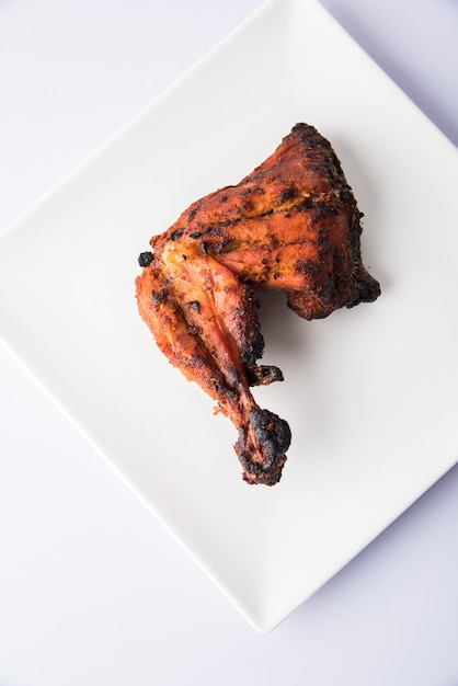 Tandoori chicken - prepared by roasting chicken marinated in yoghurt and spices in a tandoor. Leg piece served in a plate with salad over colourful or wooden background. Selective focus