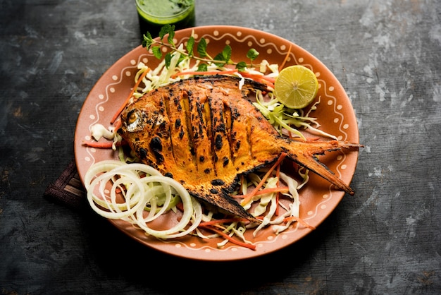 Tandoori Pomfret fish cooked in a clay oven and garnished with lemon , mint, cabbage and carrot salad. Selective focus