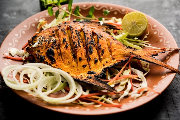 Tandoori Pomfret fish cooked in a clay oven and garnished with lemon , mint, cabbage and carrot salad. Selective focus